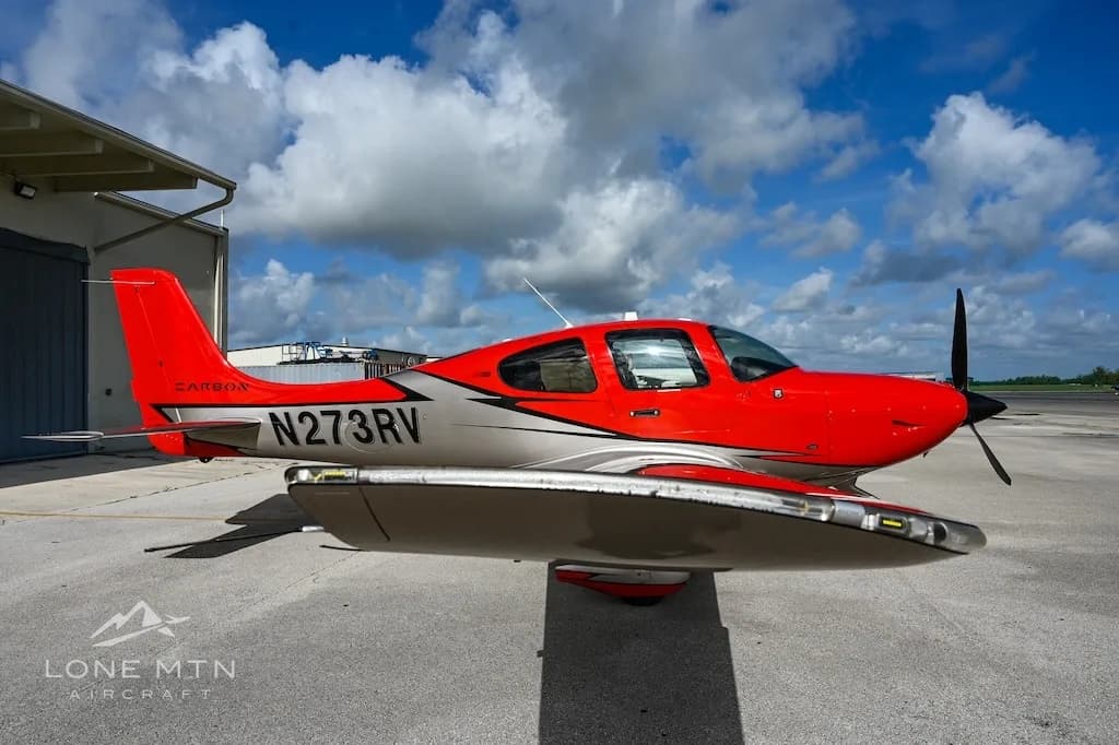 A low-angle side view of a red and silver Cirrus SR22 aircraft, registration N273RV, parked on an airport ramp.