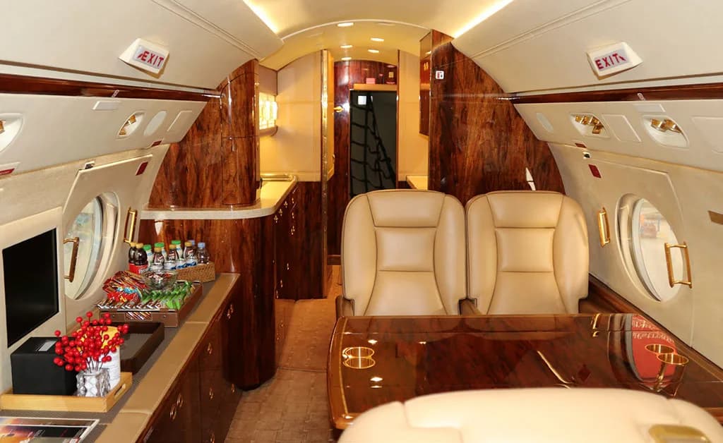A private jet's cabin interior with a dining table, two tan leather seats, and a side console with snacks and drinks.