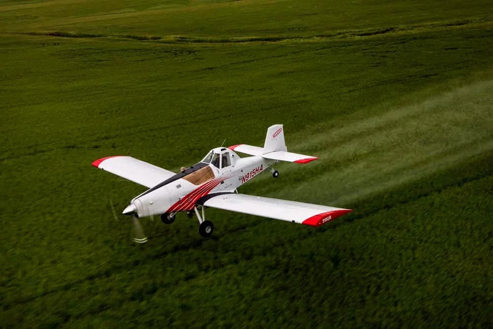 Air Tractor crop duster spraying a field with a red and white paint scheme.