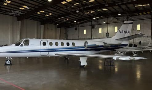 A white Cessna Citation business jet with blue stripes is parked inside a hangar, showing its tail number N51DA.