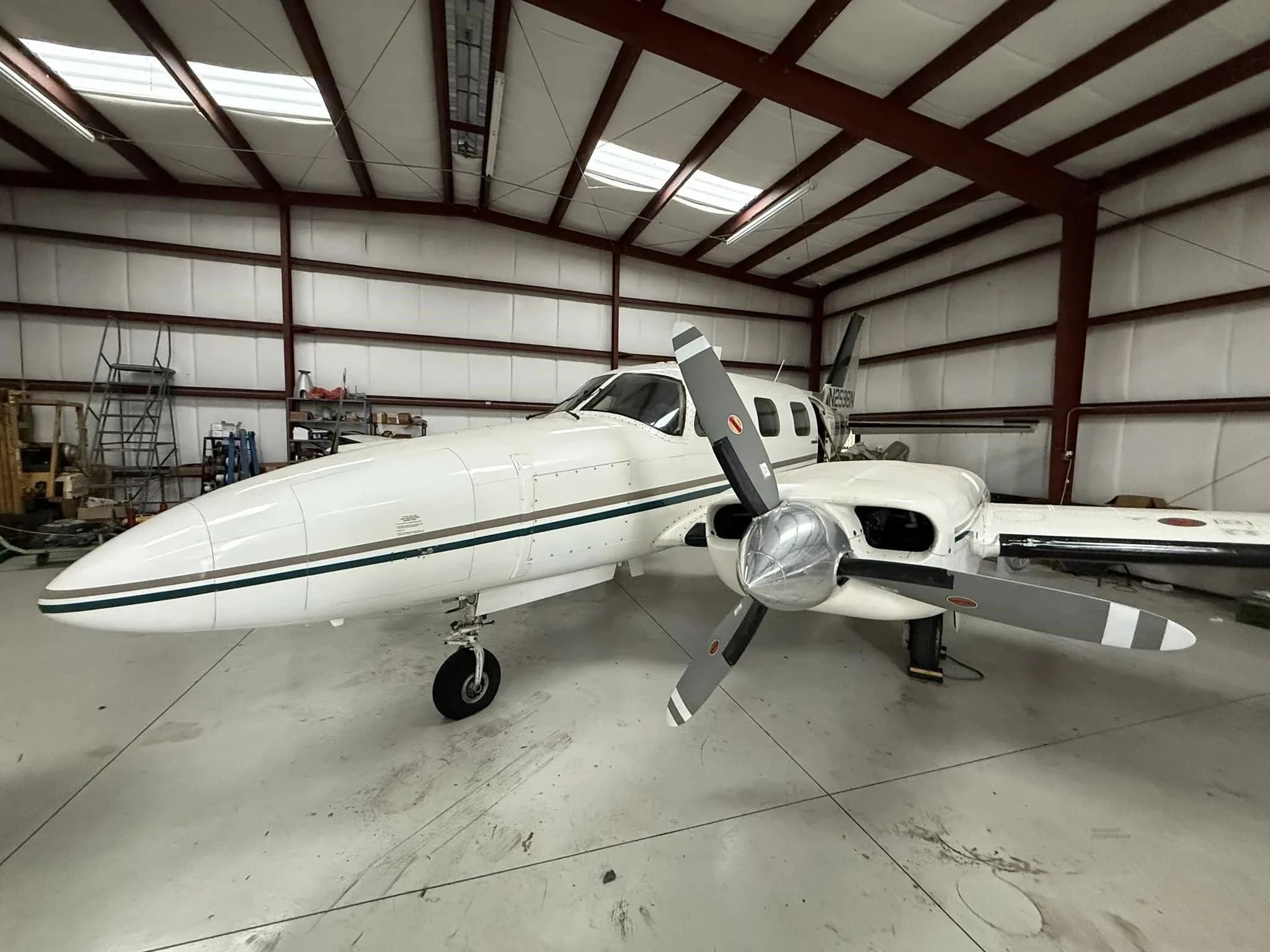 A white twin-engine Piper Navajo aircraft with green and brown stripes, seen head-on in a hangar.