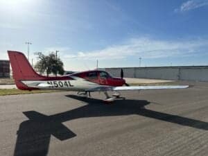 A Cirrus SR22T aircraft with a red and silver paint scheme is parked on a tarmac, showing the registration number N504L.