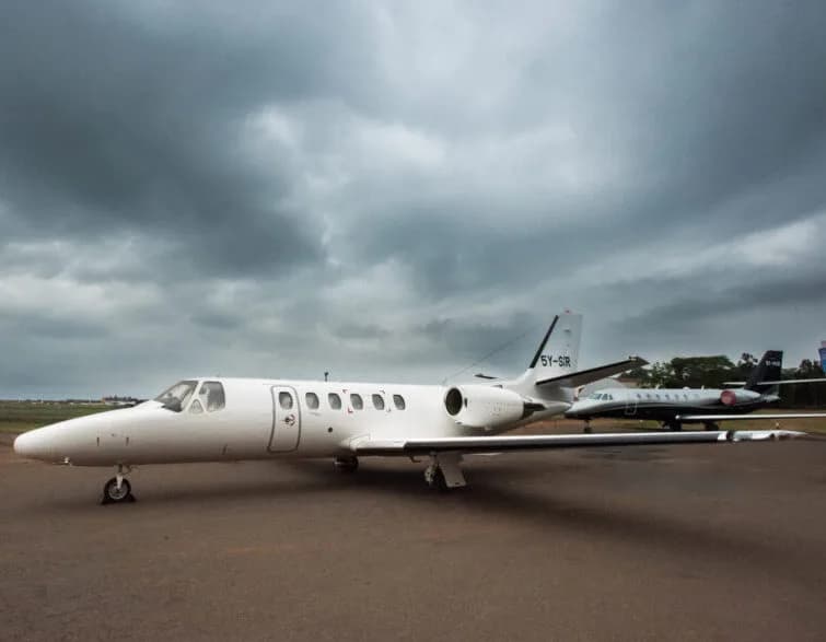 A white Cessna Citation business jet with registration 5Y-SIR parked on a tarmac under a cloudy sky, with another jet in the background.