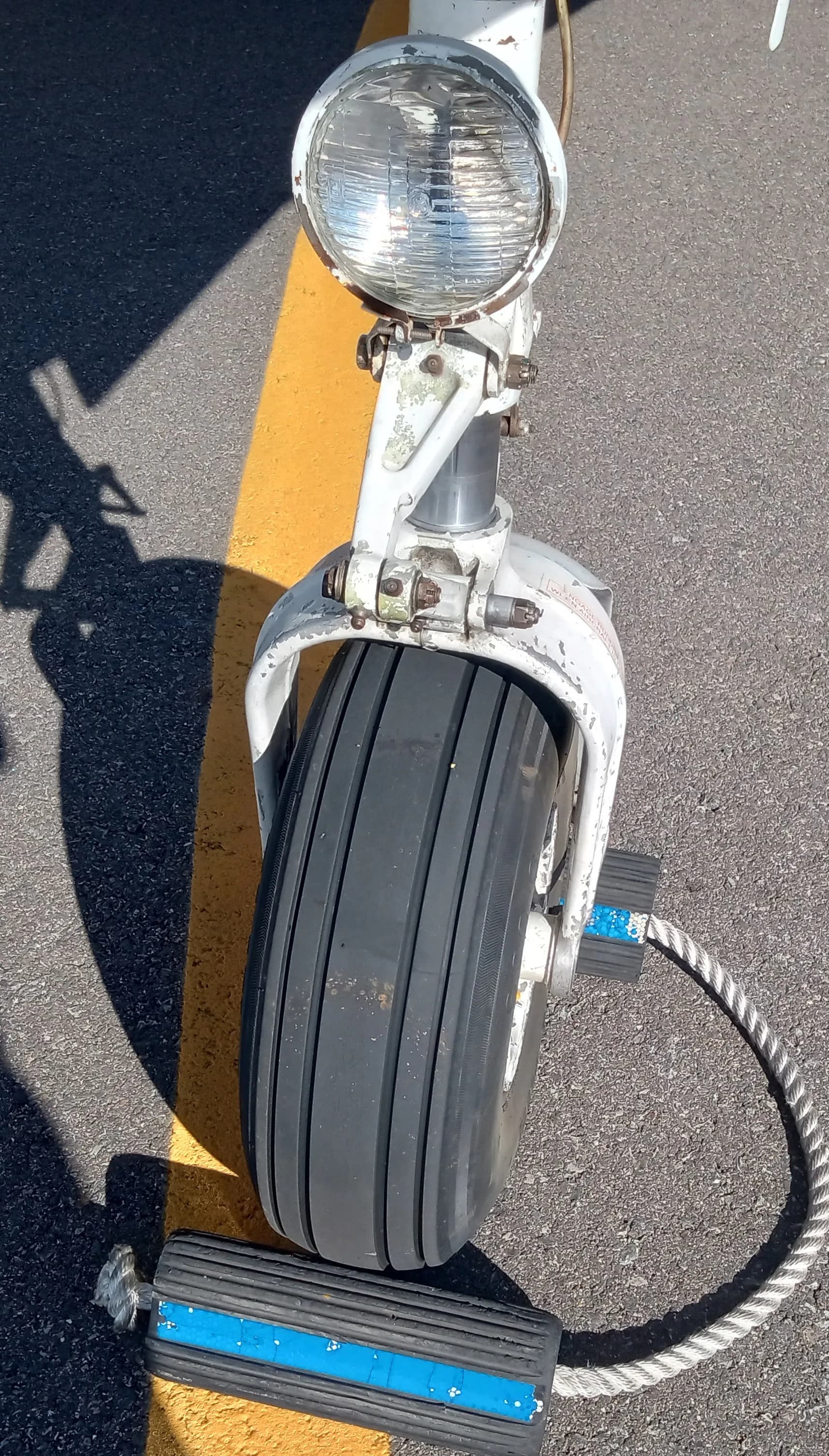 A close-up view of the aircraft's nose landing gear, wheel, and landing light on an asphalt surface.