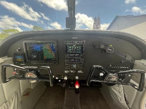 The cockpit of the Piper Cherokee 180 aircraft, showing the instrument panel with modern avionics displays and dual control yokes.