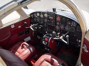 The cockpit of the Piper Apache with red leather seats and a full instrument panel.