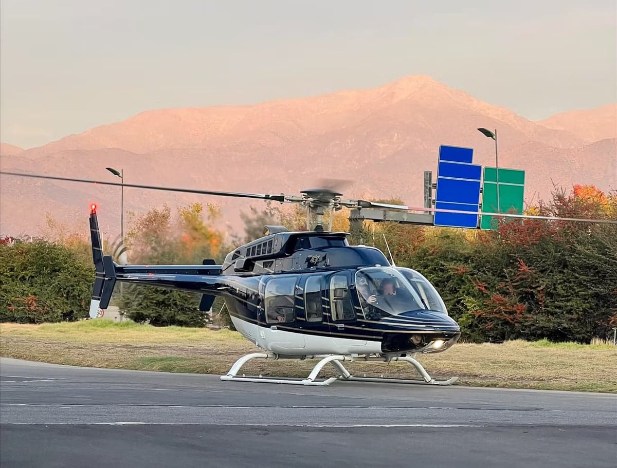 A Bell 407 helicopter in a black and white paint scheme is shown on the ground with a mountain in the background.