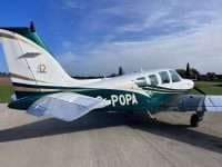 A Beechcraft Bonanza with a white and green paint scheme is parked on the tarmac.