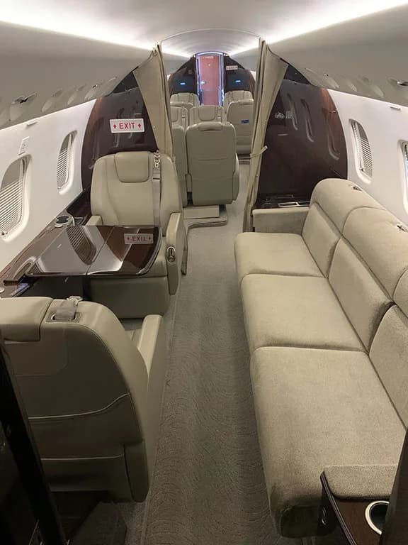 The spacious interior of the Embraer Legacy 650, featuring individual beige seats and a comfortable side couch.