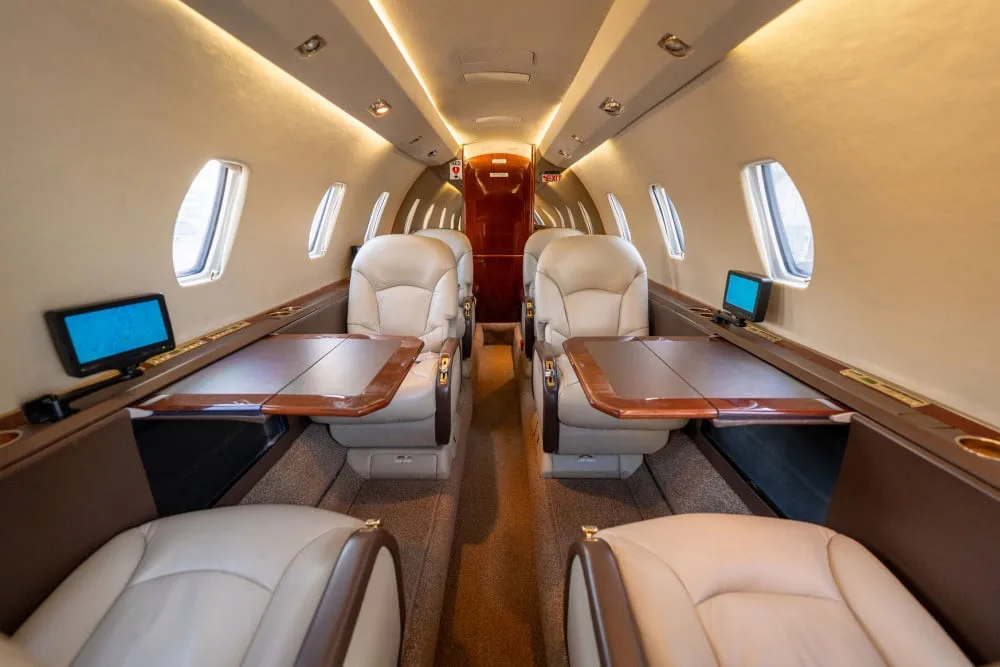 The private jet cabin interior with beige leather seats and wooden tables extended for passengers.
