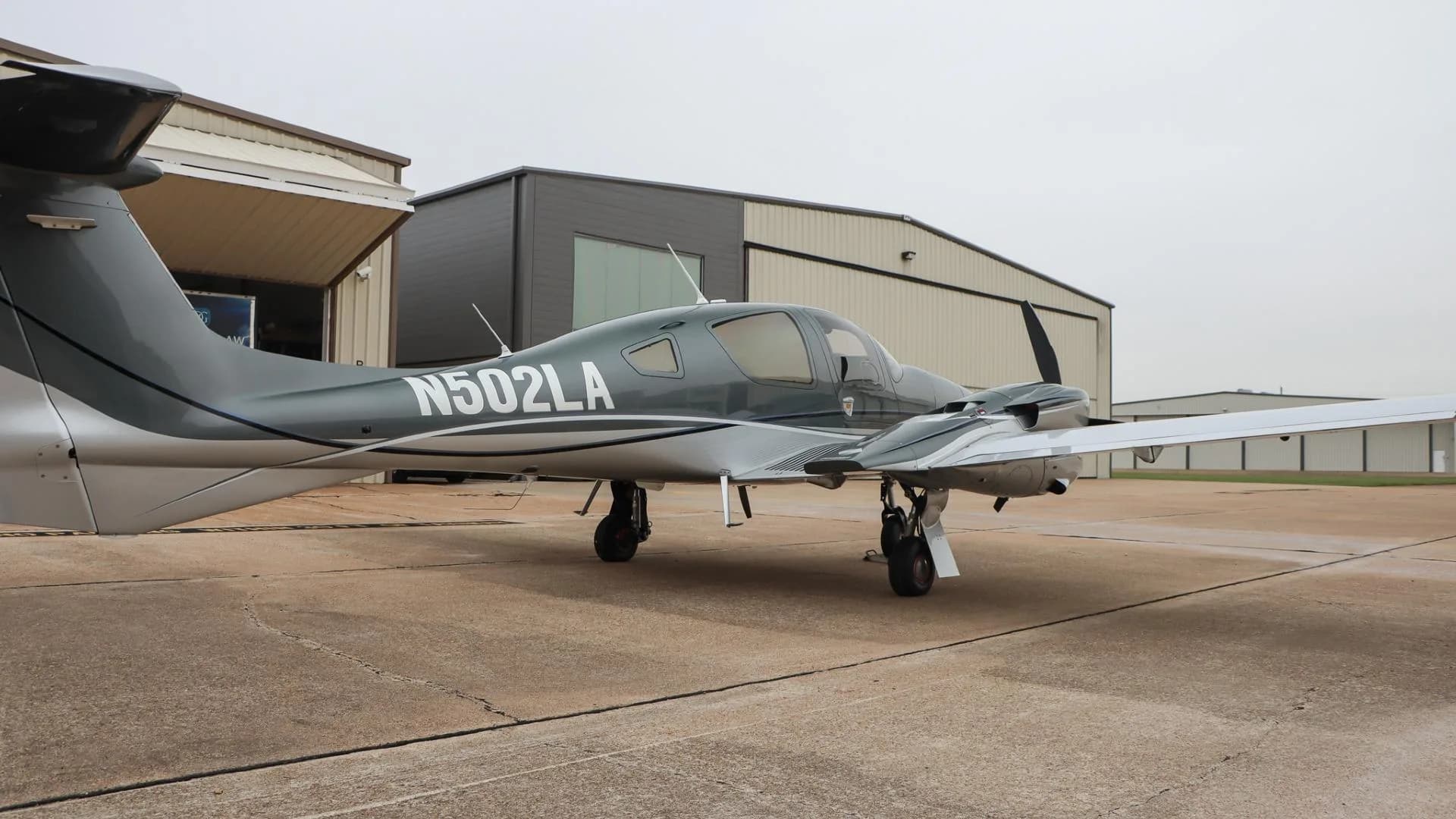 A rear-side view of the gray and silver Diamond DA62 aircraft, N502LA, parked on an airport tarmac.