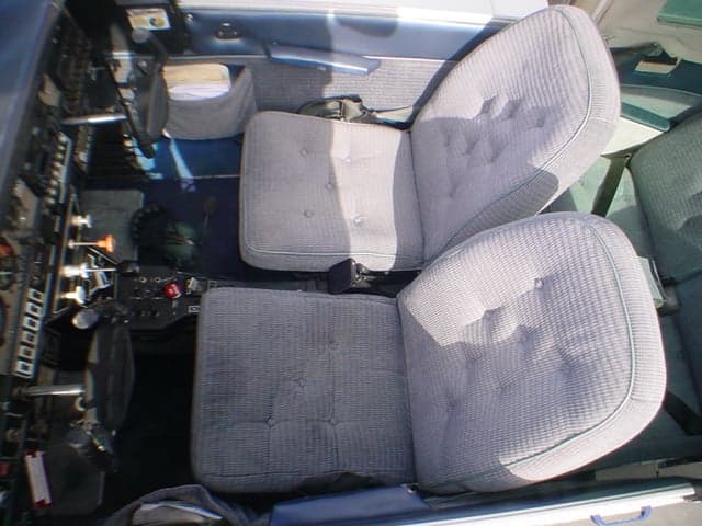 The gray upholstered front seats and blue carpeted interior of a Grumman AA-5 Traveler aircraft.