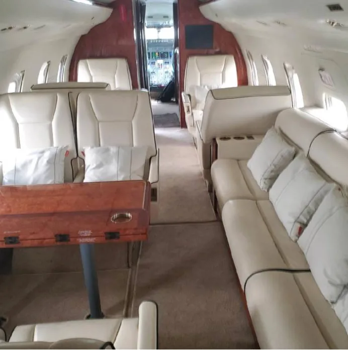 Aircraft interior with tan leather seats and a wooden table.