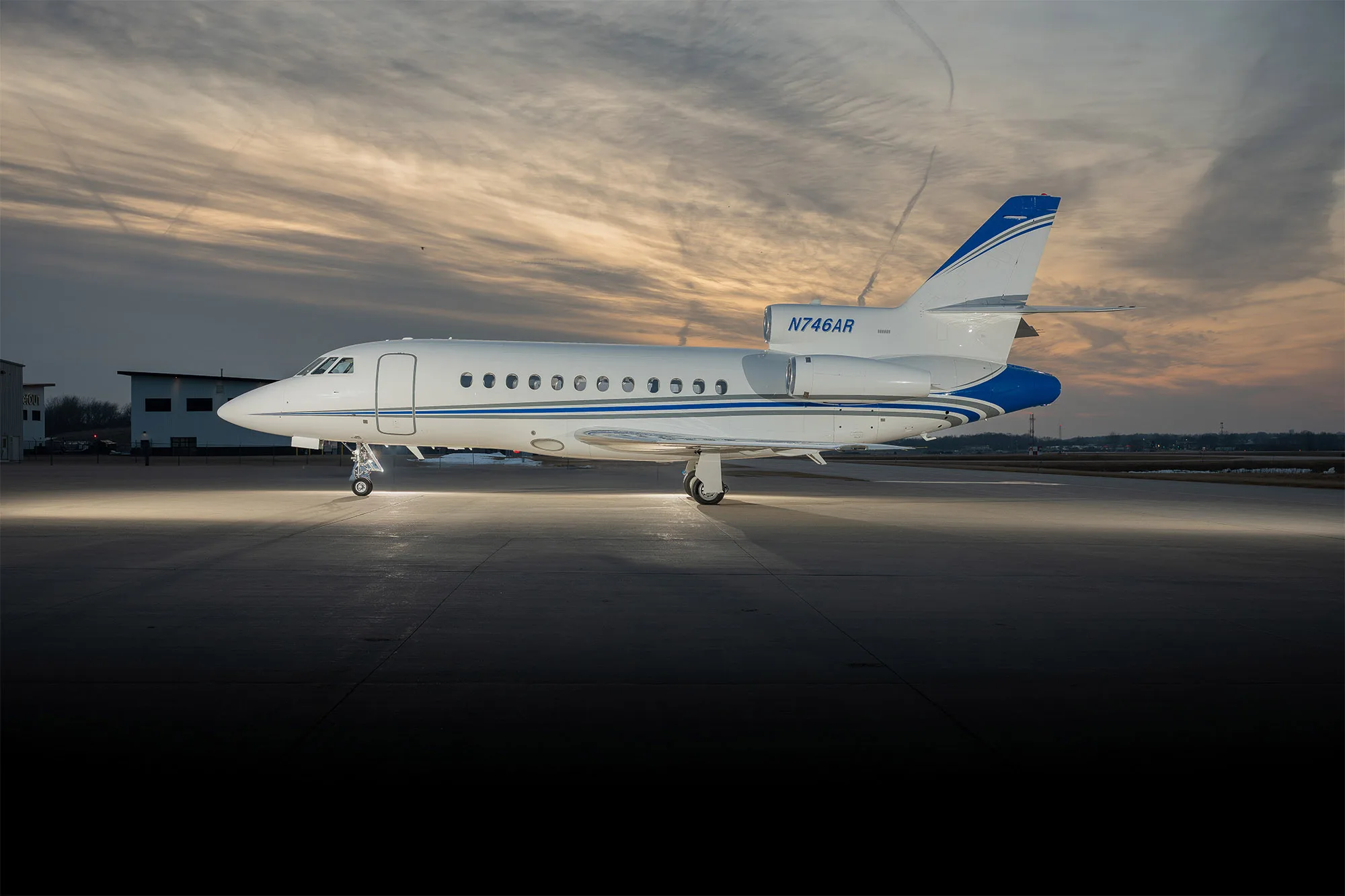 Side view of a white and blue jet with registration N746AR on the tarmac at sunset.