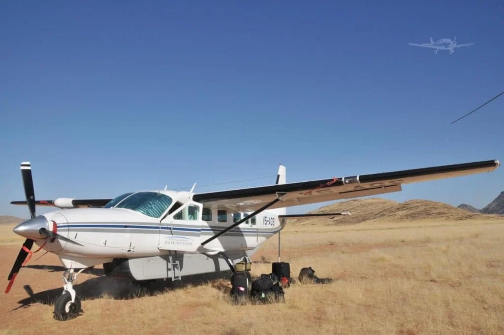 A Cessna Caravan aircraft is parked on a grassy field under a clear blue sky.
