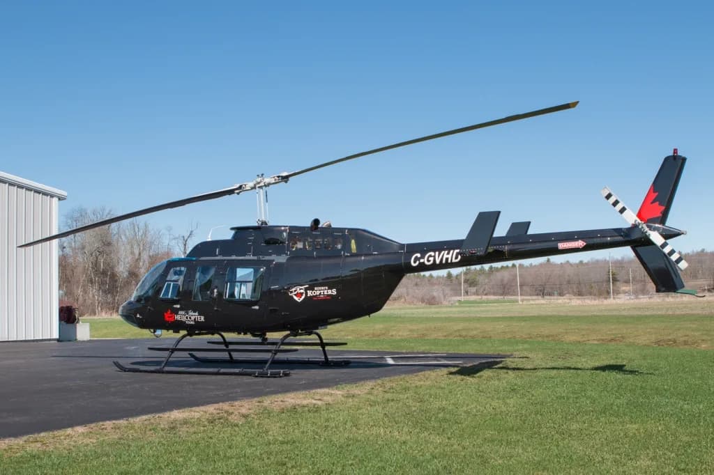 A black Bell 206 helicopter with registration C-GVHD is parked on a tarmac next to a white hangar.