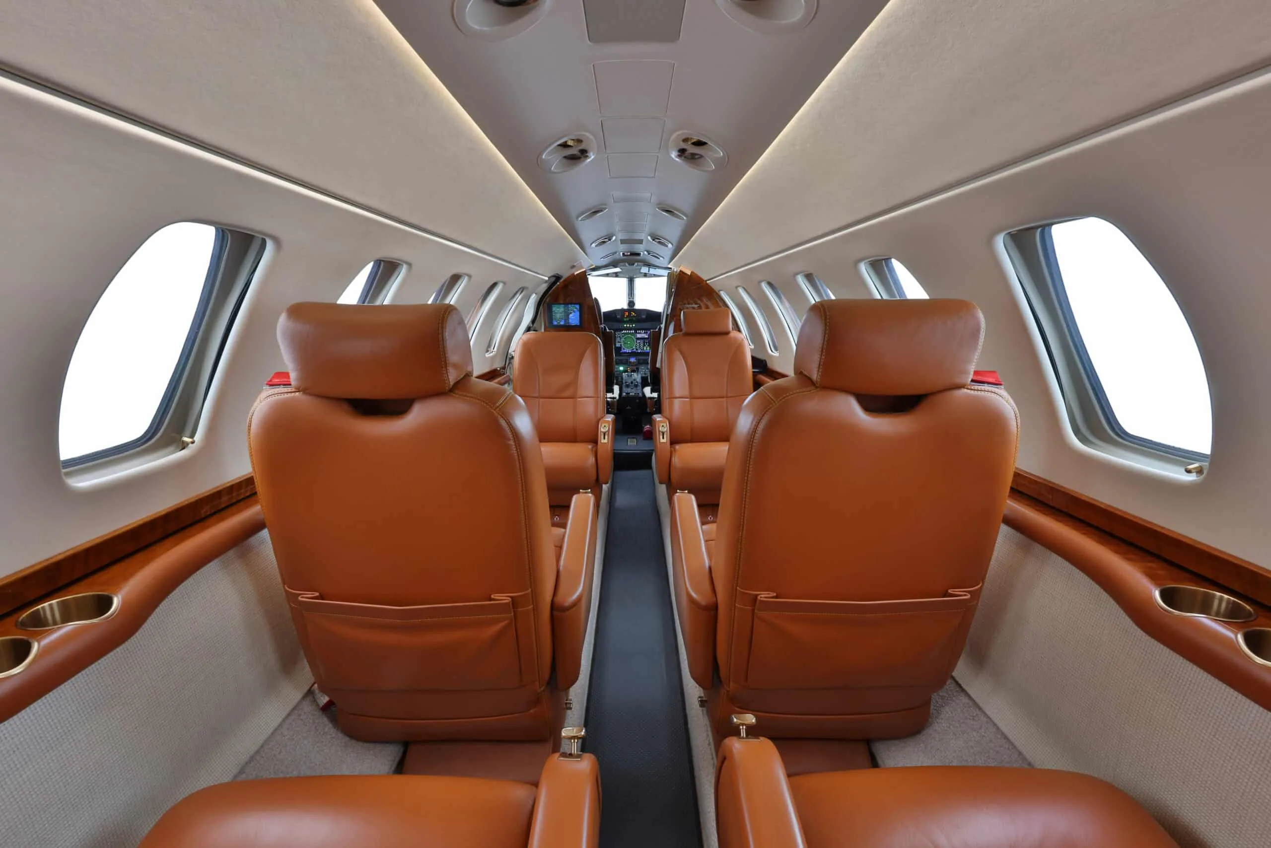 Aft view of a private jet cabin with tan leather seats facing forward towards the cockpit.