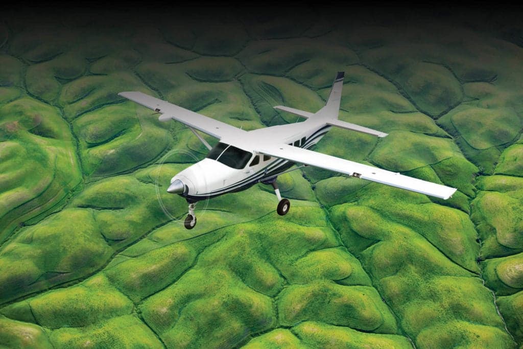 A Cessna Caravan flying over a green, hilly landscape.