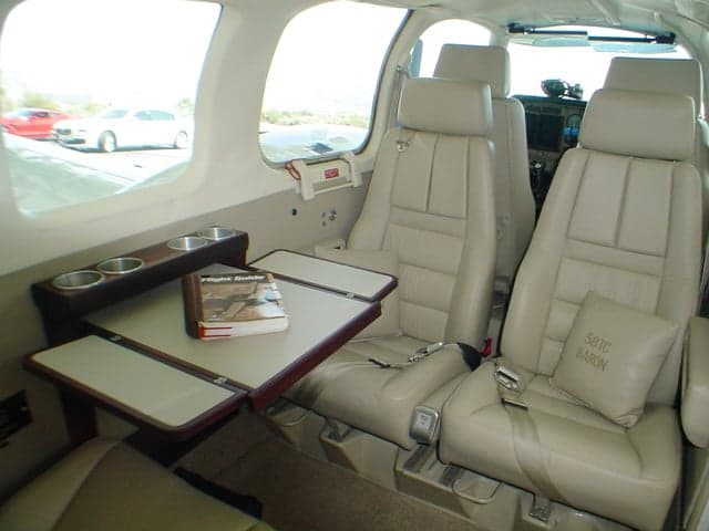 The tan leather interior of a Beechcraft Baron 58TC cabin features a fold-out table with a book and cup holders.