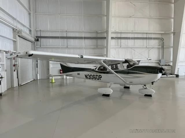 A white and green Cessna 172S aircraft with registration N306DP is parked inside a hangar.