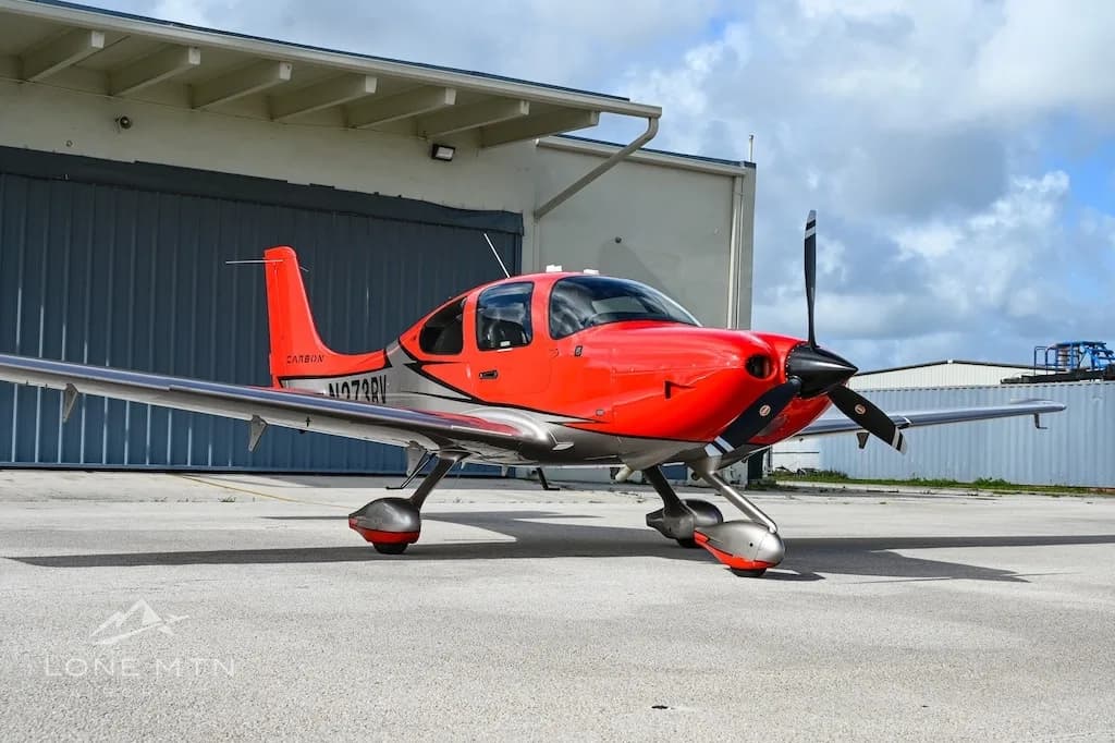 A red and silver Cirrus SR22 aircraft, registration N273RV, parked on an asphalt ramp in front of a hangar.