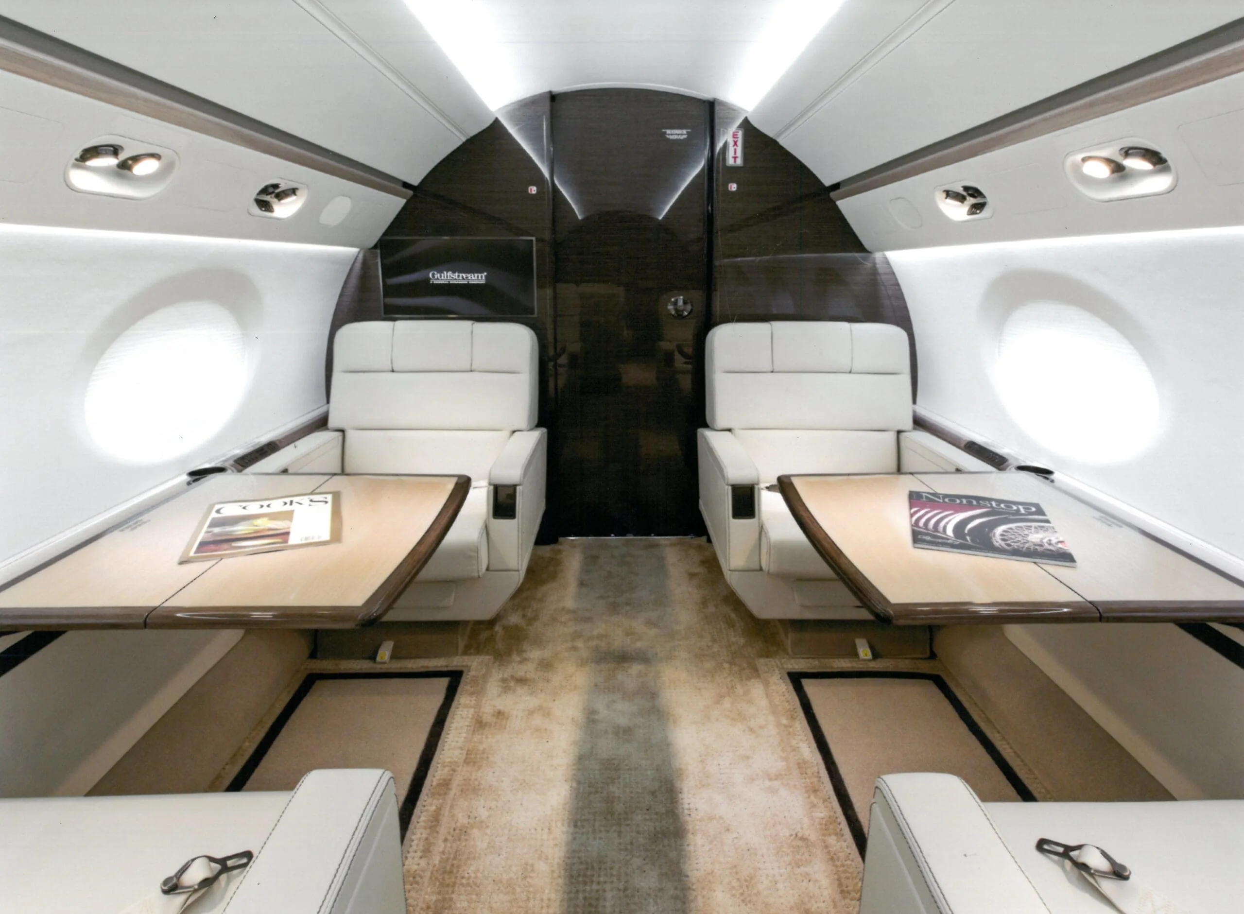 View of the aircraft cabin with white leather seats and tables.