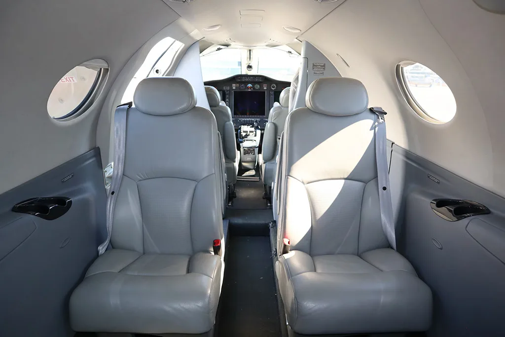 The light gray leather seats in the cabin of a private jet, with a view towards the cockpit in the distance.