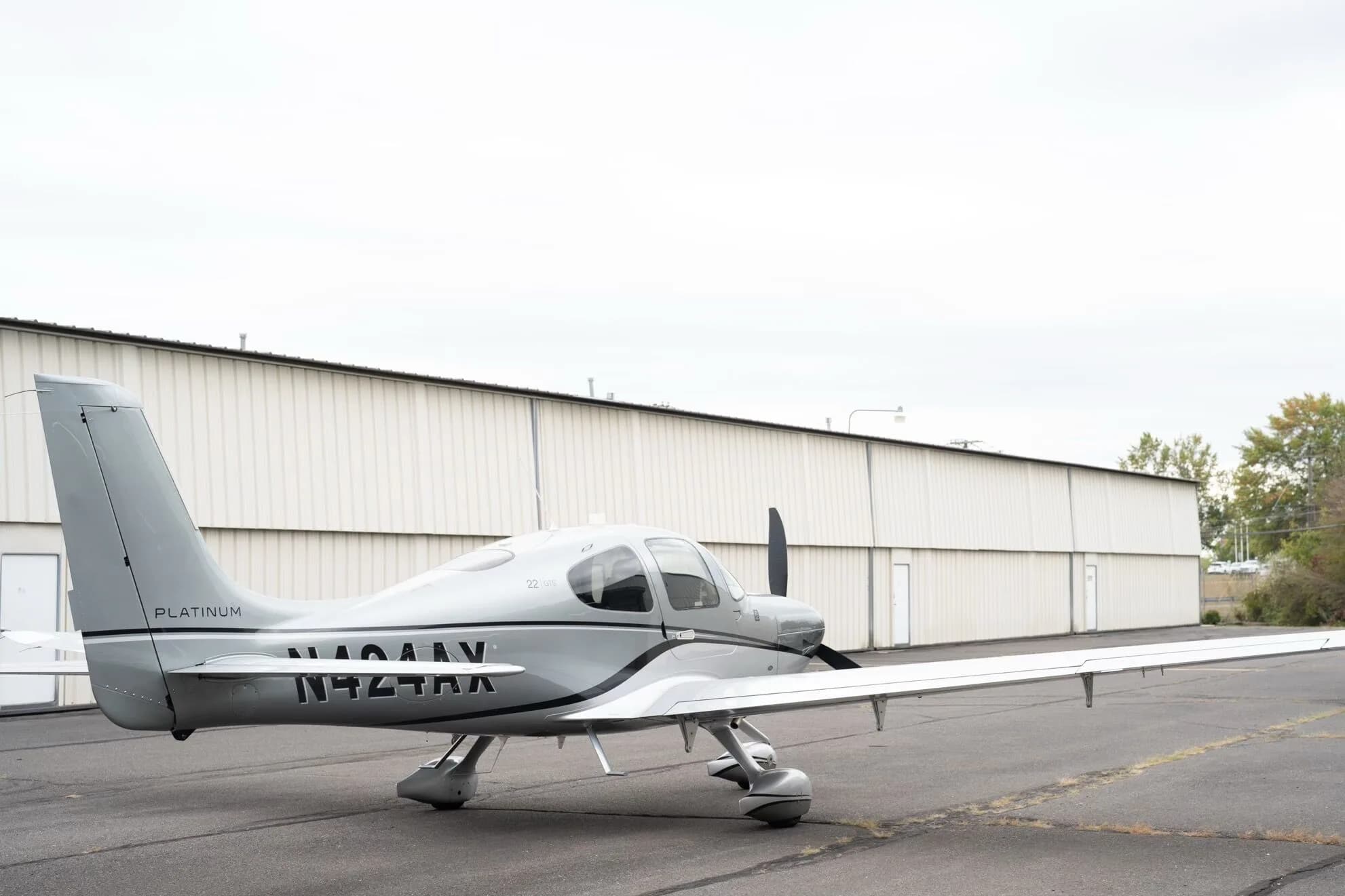 A silver Cirrus SR22 GTS Platinum aircraft, N424AX, is seen from a rear-quarter view on an asphalt tarmac.