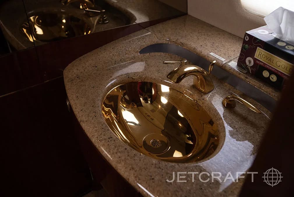 A gold-colored sink in the lavatory of the jet.