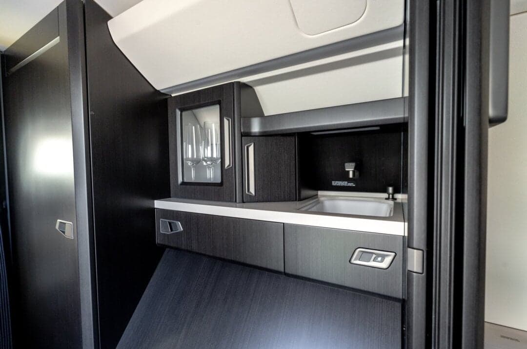 A close-up of the dark wood galley area in a private jet, featuring a sink and glassware storage.