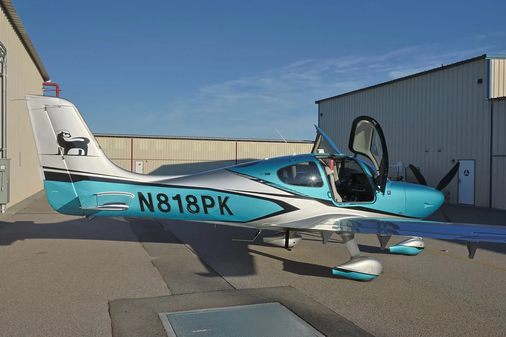 A side view of a teal and silver Cirrus SR22T GTS aircraft (N818PK) with its doors open, parked on an airfield.