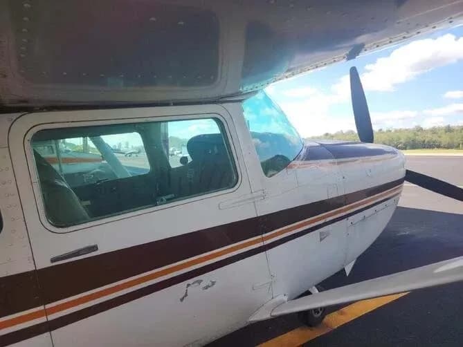 A close-up side view of the cockpit and propeller of a white and brown Cessna Skylane RG II aircraft.