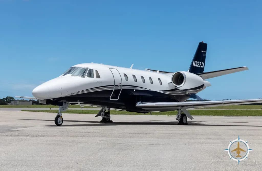 A white and blue Cessna Citation Latitude business jet with registration N327JA on a tarmac under a clear blue sky.