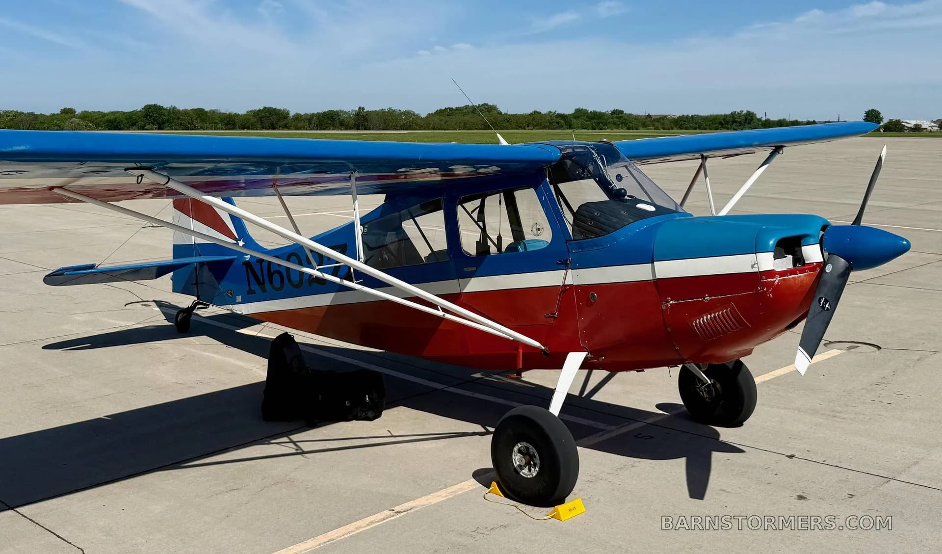 A red and blue high-wing aircraft with registration N602Z is parked on a tarmac under a blue sky.