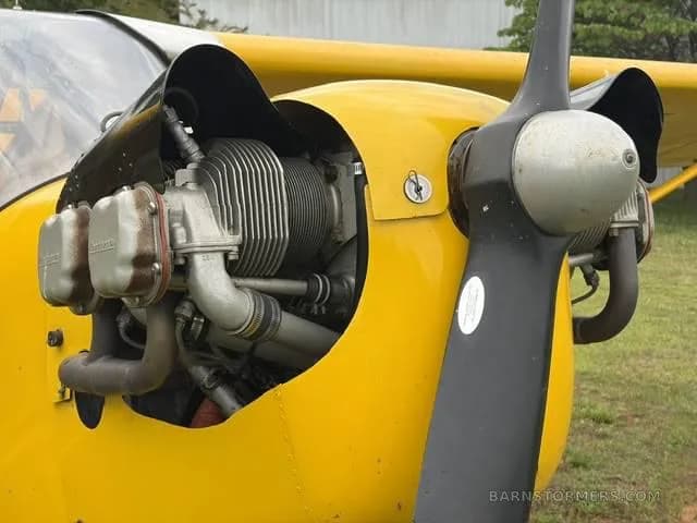 A close-up view of the exposed engine and propeller of a yellow aircraft.