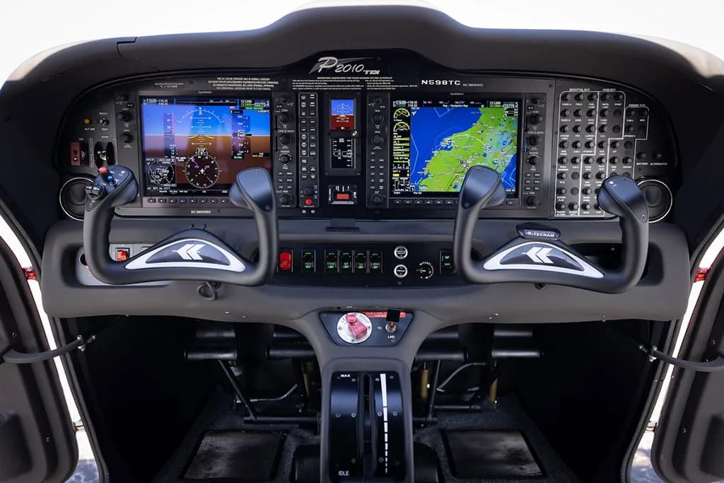 The modern glass cockpit of a Tecnam P2010 aircraft, featuring multiple display screens and dual yokes.