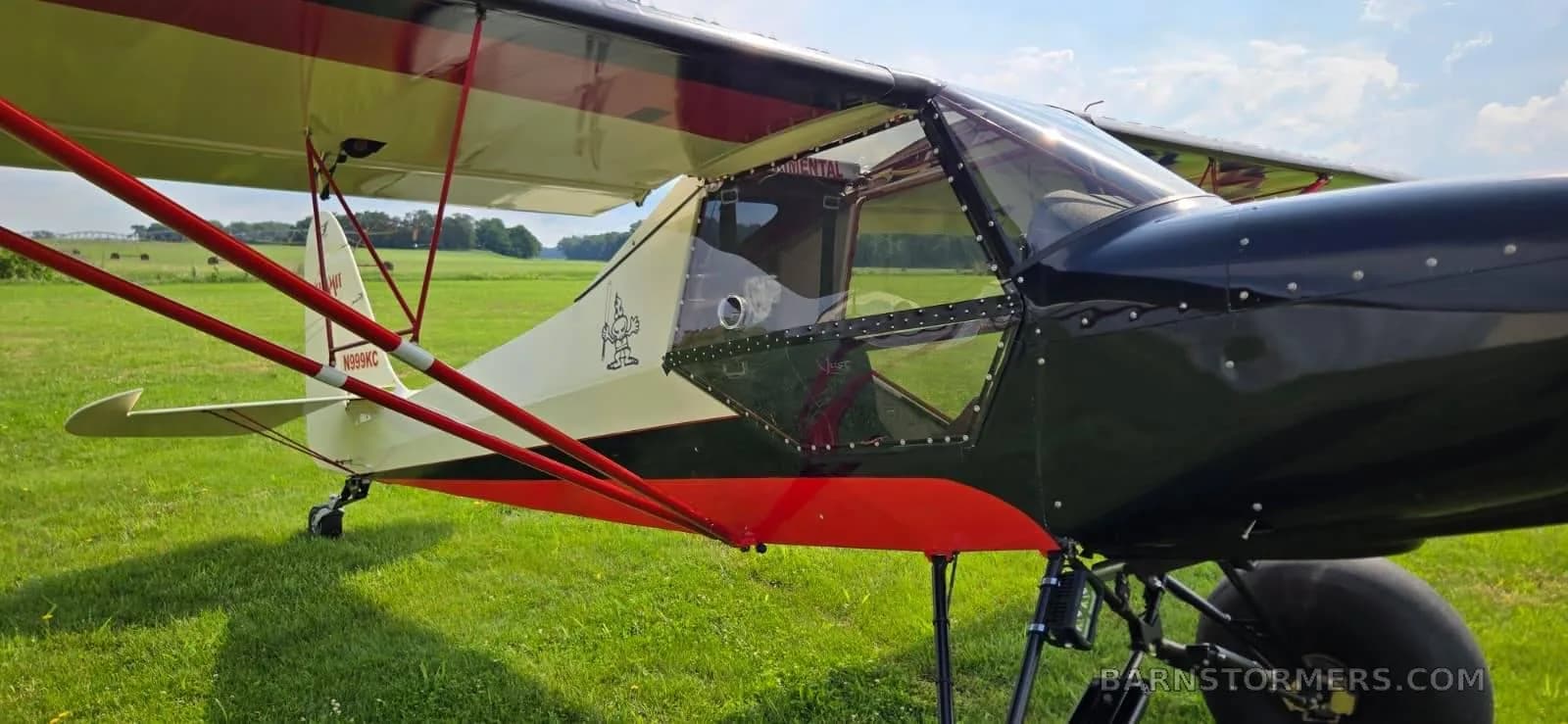A close-up view of the black, red, and cream bush plane's cockpit and fuselage, showing its large tires and the N-number on the tail.
