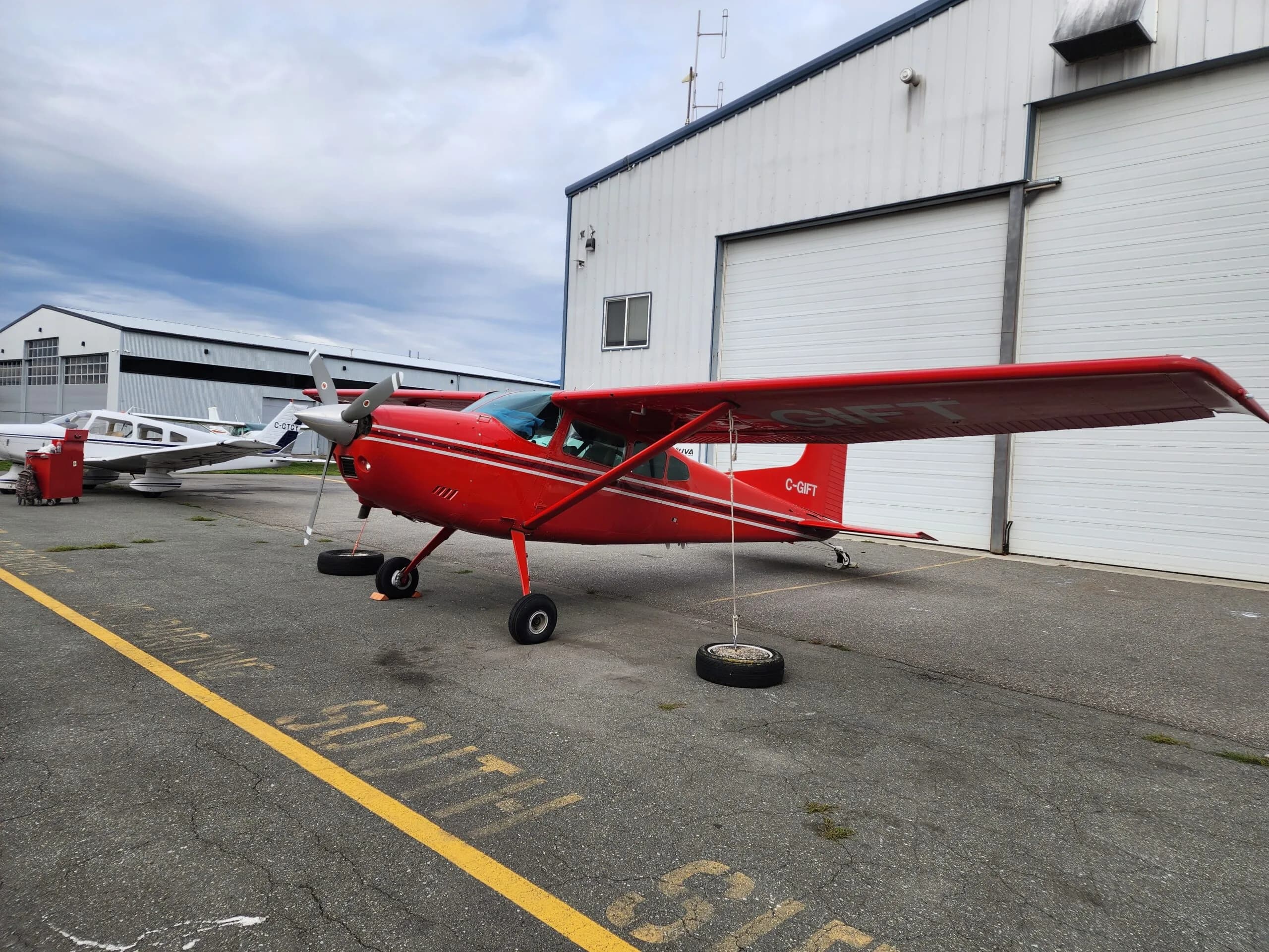 A red and white Cessna aircraft with registration C-GIFT parked in front of a hangar.