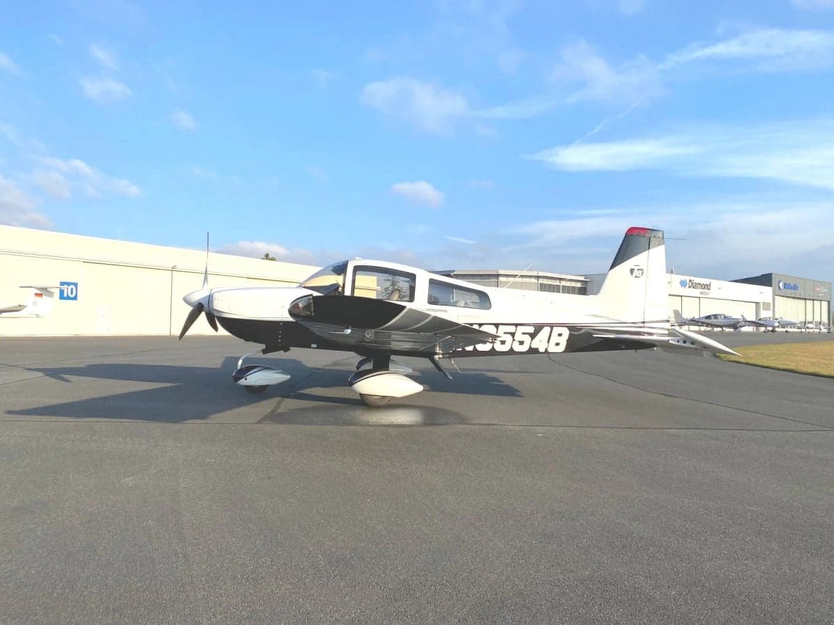 Rear view of a white aircraft on the tarmac in front of hangars.