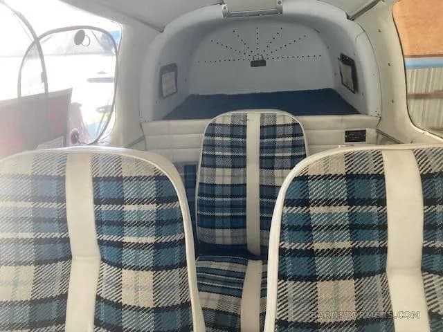 The aircraft's interior cabin features blue and white plaid seats and a small rear cargo area.
