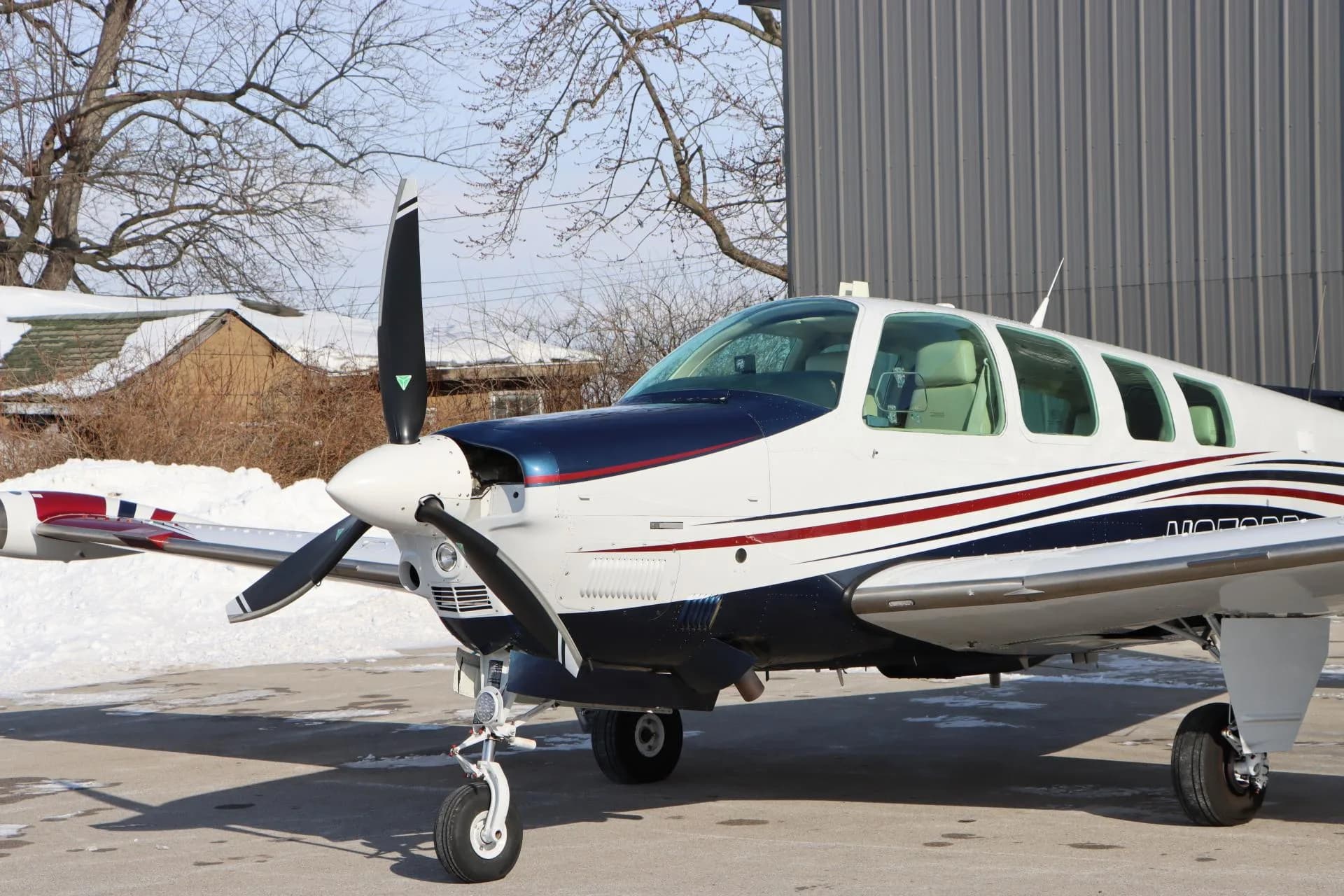 Close-up side view of the front section of a white, blue, and red single-engine aircraft, showing the propeller and cockpit.