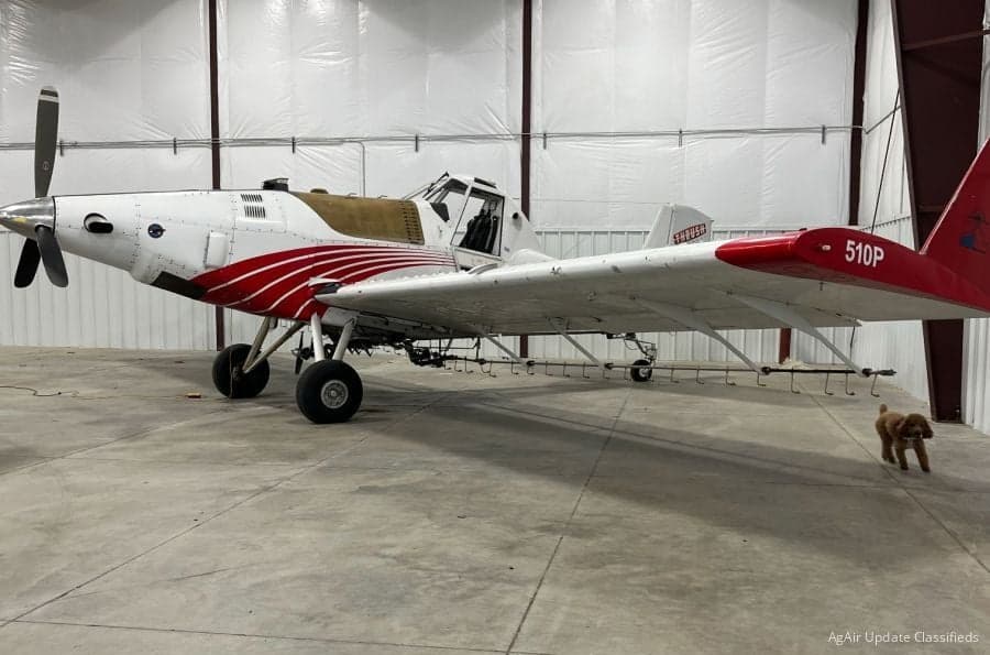 A white and red Air Tractor 510P crop duster is parked in a hangar.