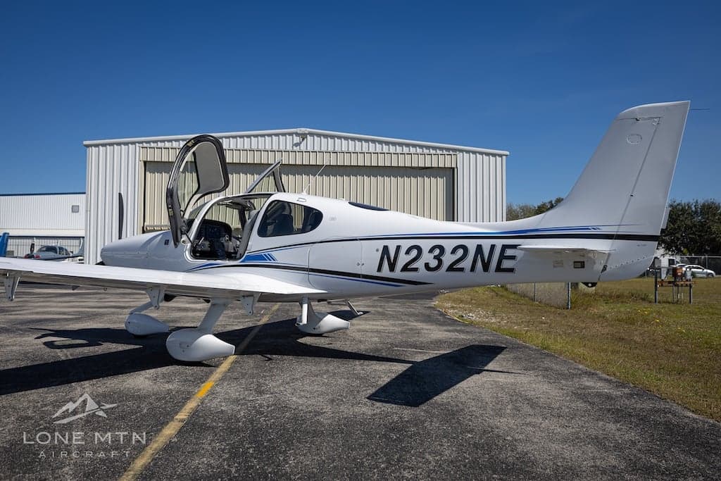 Cirrus SR22T aircraft N232NE parked near a hangar with open doors, side view.