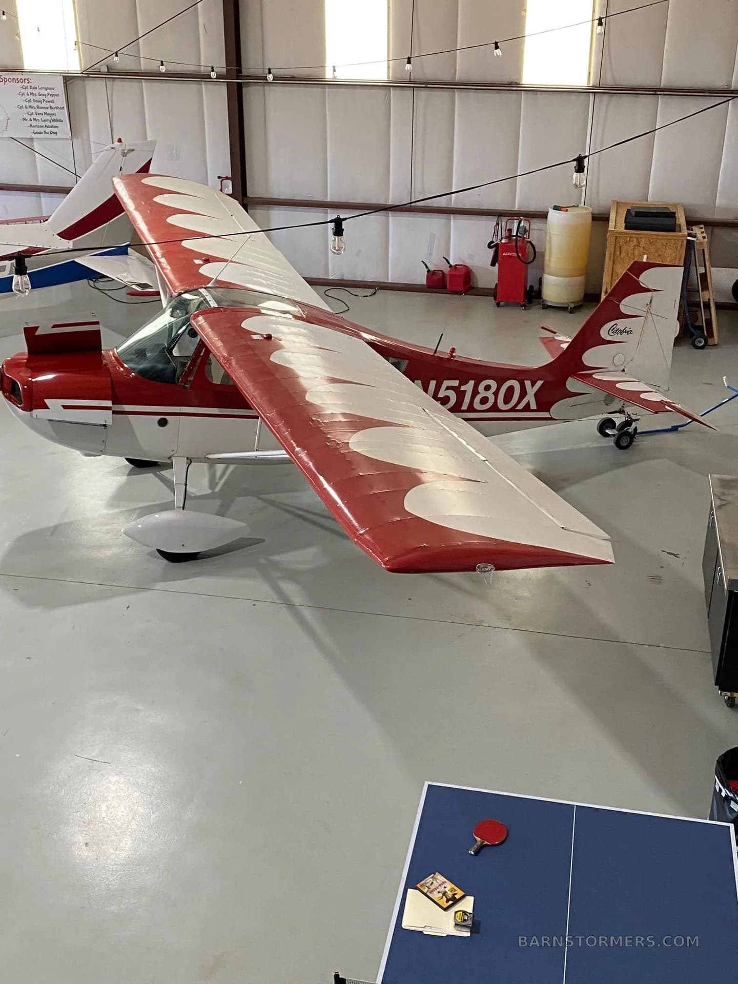 An overhead view of a red and white single-engine aircraft with registration N5180X parked in a hangar.