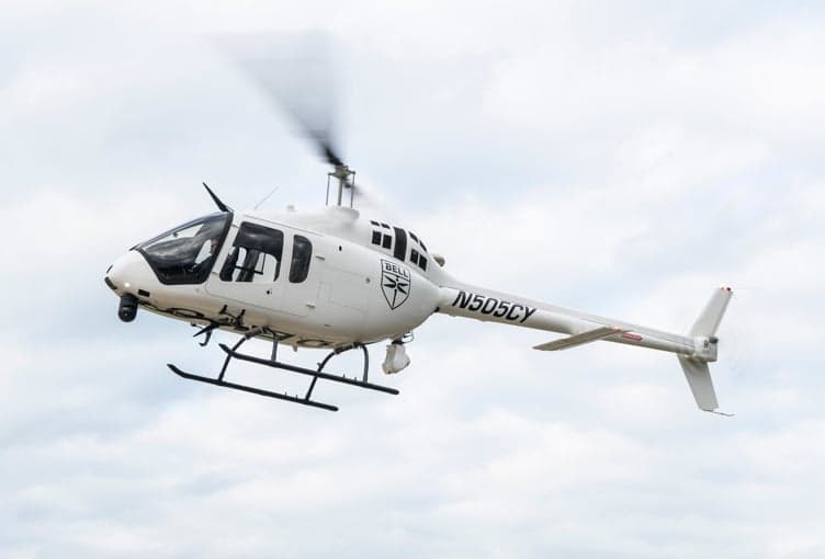 A white Bell 505 helicopter with registration N505CY in flight against a cloudy sky.