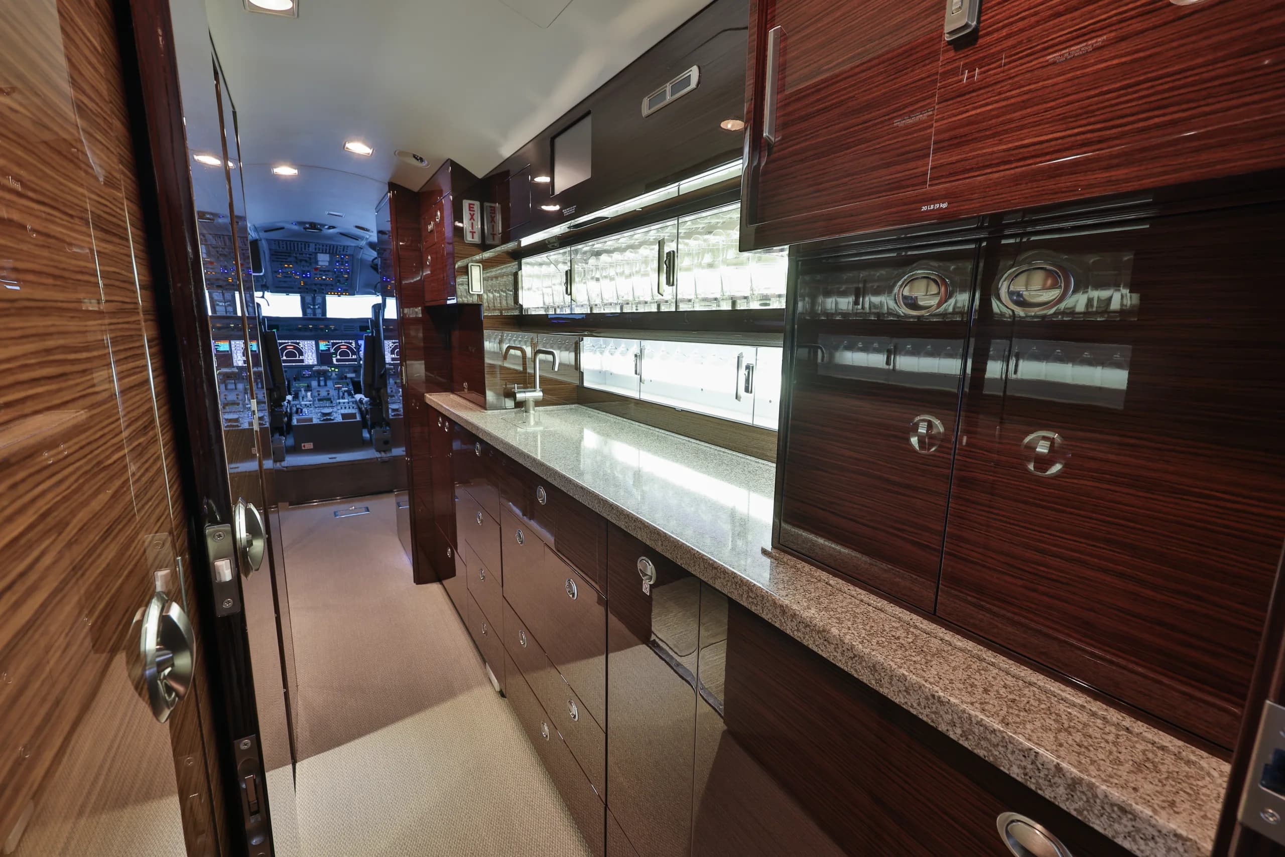 A well-appointed aircraft galley with dark wood cabinetry, a granite countertop, and a view into the cockpit.