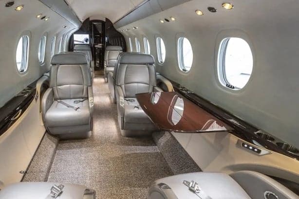 The jet's interior has gray leather seats, a gray carpet, and a wooden table.