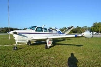 A Beechcraft Bonanza sits on a grassy field in the sun.