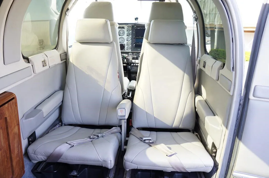 The light gray leather passenger seats of a Beechcraft Baron 58 are visible, looking towards the cockpit.