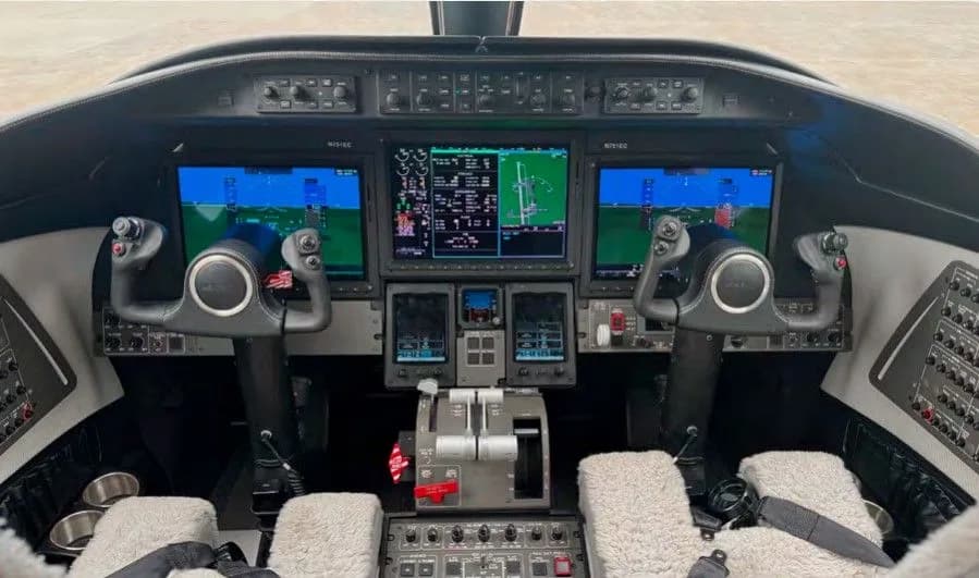 The cockpit of a business jet, featuring multiple large display screens and dual yokes.
